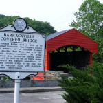 covered bridge painted red with a white historic marker by the bridge
