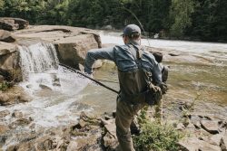 man fishing in a river with waterfalls in the background