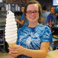 girl in blue tie dyed shirt holding a vary large vanilla ice cream cone