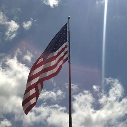 American Flag blowing in the wind with a blue sky and clouds
