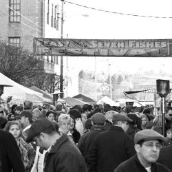black and white photo of an outdoor festival with lots of people standing under a banner
