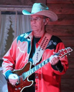 man wearing a cowboy hat and red & black western shirt holding a guitar