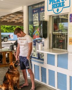man standing in front of an ice cream shop with a dog 