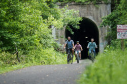 three guys on bicycles coming through a tunnel 