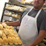 man in white apron holding a tray of baked pepperoni rolls