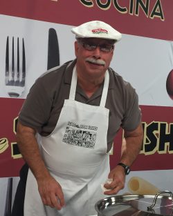 man wearing white apron and hat preparing food during a cooking demonstration