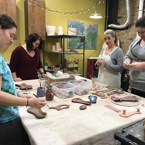 4 women rolling out clay at a table surrounded by other art supplies