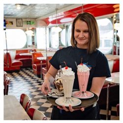 girl holding a tray of milkshakes in a diner