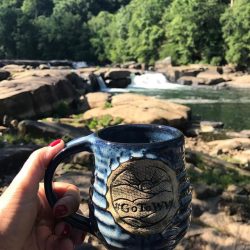 woman holding a blue mug with waterfalls and trees in the background
