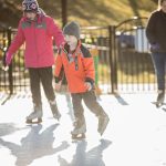 girl in pink coat and boy in orange coat ice skating