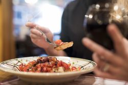 person holding a forkful of bruschetta and glass of red wine