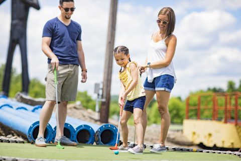 mom, dad and daughter playing mini golf