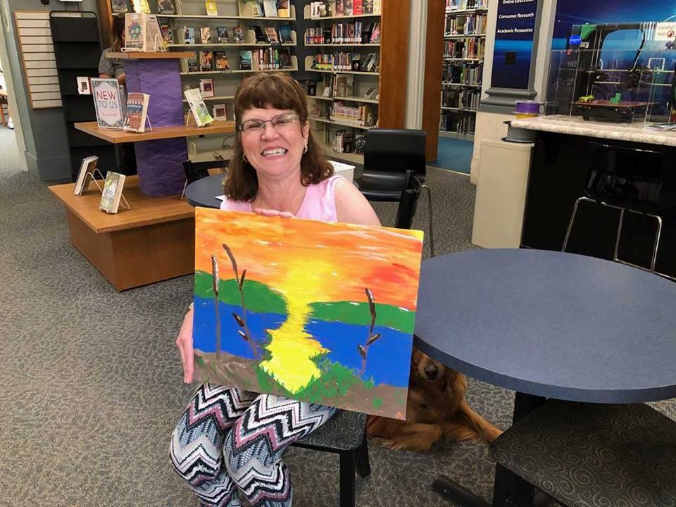 woman holding a painting of a sunset