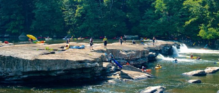 kayakers on large rock looking over falls