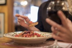 person holding a class of red wine and eating bruschetta from a bowl