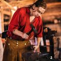 man dressed in 18th C clothes working in a blacksmith shop