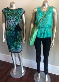 mannequins wearing a green dress and green top with black pants holding a green purse