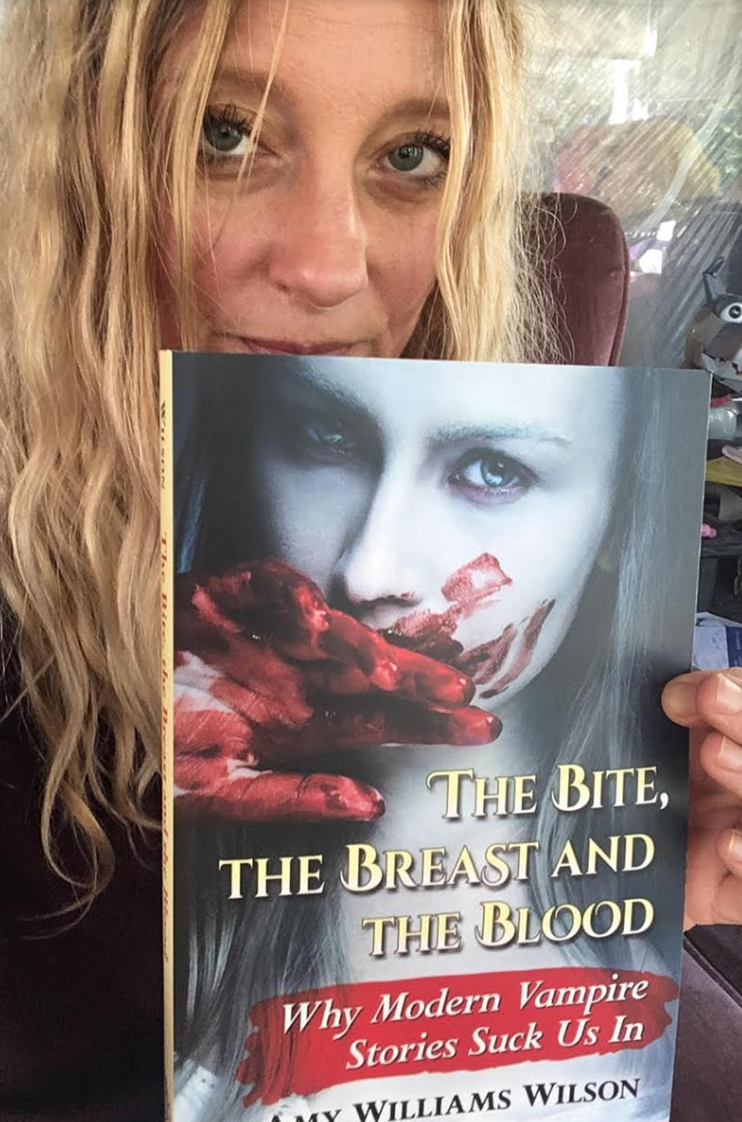 long blond haired woman holding a book about a vampire
