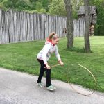 girl holding a stick trying to roll a wooden ring outside