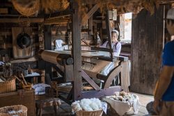 woman dressed in 18th century clothing at a loom with baskets of shaved wool around