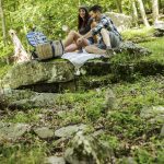 man and woman sitting outside on large rocks in the woods having a picnic