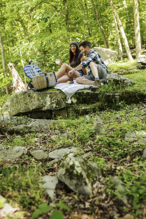 man and woman sitting outside on large rocks in the woods having a picnic