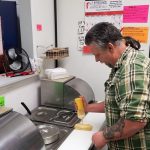 man in green shirt adding mustard to a hot dog in a restaurant kitchen
