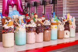 row of milkshakes topped with candy bars, cookies and sprinkles