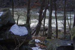 large rocks dusted with snow with bare trees and waterfalls in the background