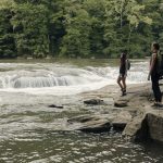 2 women standing on large rocks looking a water falls