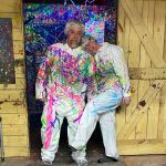 a man and woman wearing white overalls covered in paint splatters