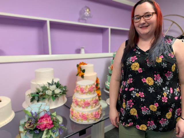 woman in floral print shirt standing by decorated layer cakes