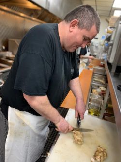 man in black t-shirt and white kitchen apron cutting chicken