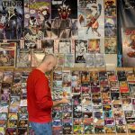 man in red shirt and jeans standing in front of racks of comic books