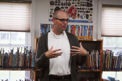 man with white shirt and grey sweater standing in front of racks of books