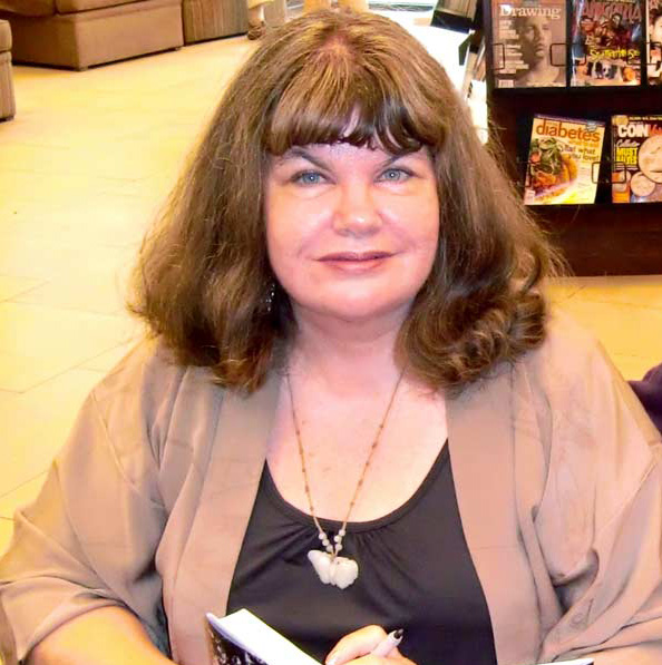 woman with shoulder length brown hair holding a book while sitting in a book store