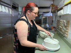 woman in black apron icing a cake with white icing