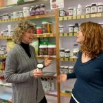 2 women talking as they stand in front of selves of health care supplements