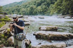 man holding a fishing rod with waterfalls in the background