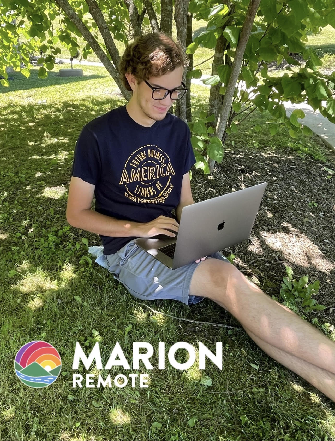 man sitting under tree holding a laptop
