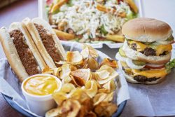 table with hot dogs with sauce, curly fries and cheese sauce, a double-stacked hamburger and steak salad