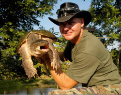 man wearing a green shirt and large hat holding a giant snapping turtle