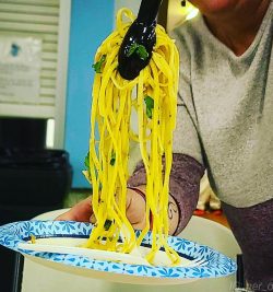 tongs scooping linguine on a paper plate