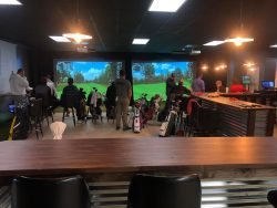 people in a bar-like setting with a golf simulator