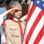 young boy scout holding the American flag and saluting