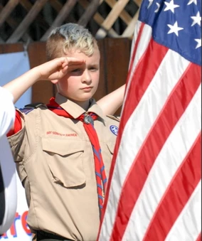 young boy scout holding the American flag and saluting