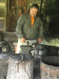 man in 18th-century clothing working in a blacksmith shop