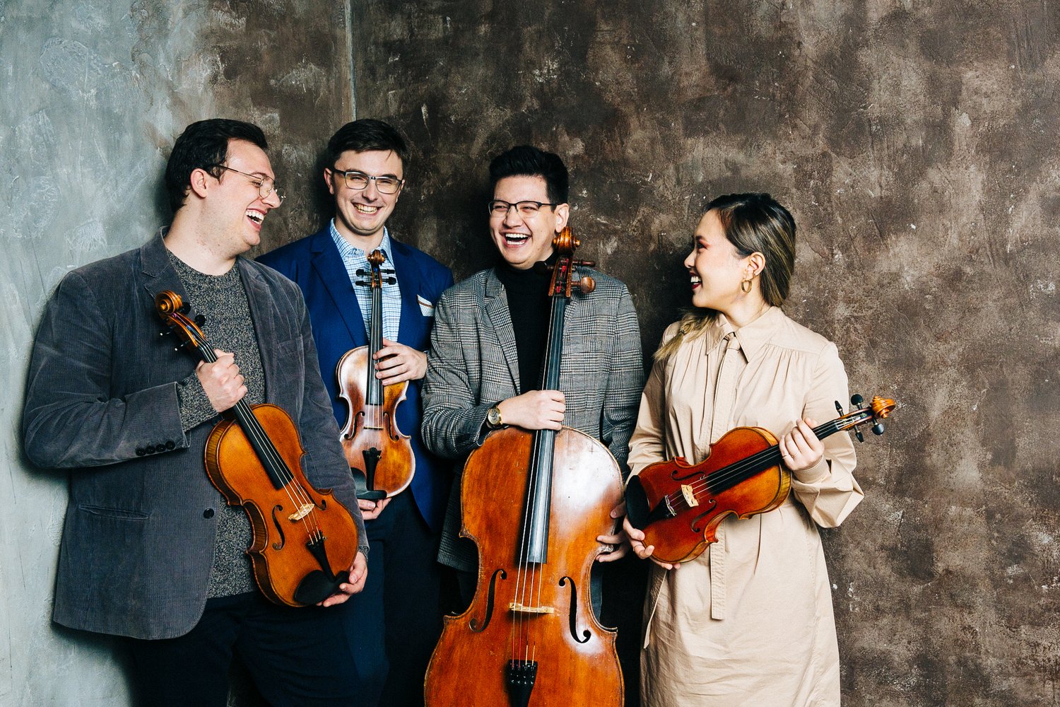 3 men and 1 woman holding string instruments laughing