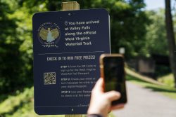 someone holding a phone to scan a QR code from a sign promoting WV's waterfall trail