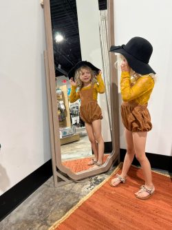 young girl looking in a mirror while trying on clothes and a hat